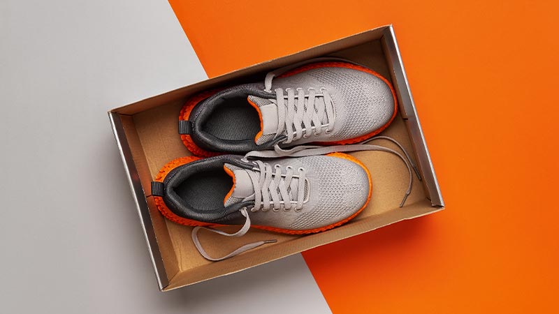 Sapatos de corrida novos numa caixa aberta, vista de cima, num fundo branco e laranja